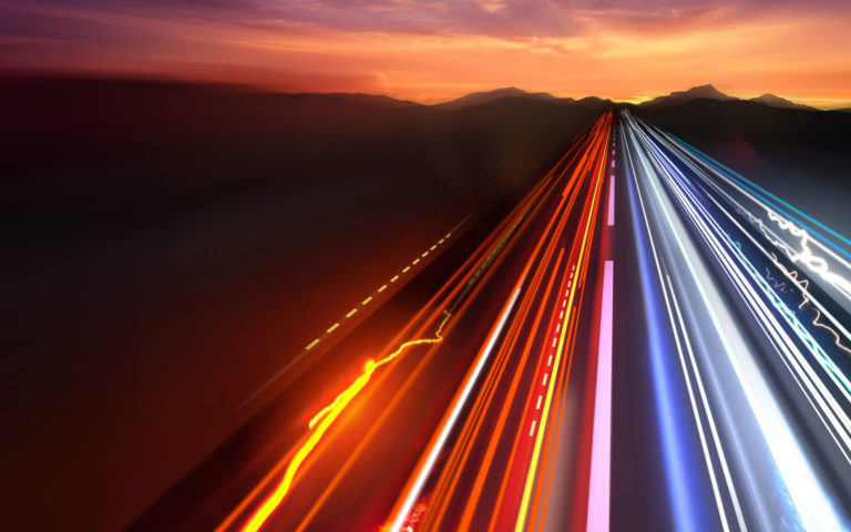 road with car lights trailing and mountains in background